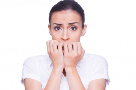 Terrified woman. Terrified young woman in formalwear looking at camera and biting nails while standing isolated on white