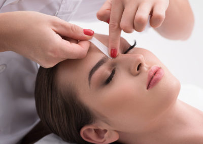 Young woman tweezing her eyebrows in beauty saloon